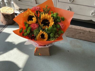 Golden Glow - Brighten someone's day with the `Golden Glow` arrangement, featuring a stunning sunflower mix with seasonal blooms. Complemented by lush green foliage, this arrangement brings a touch of nature's radiant beauty into any space.